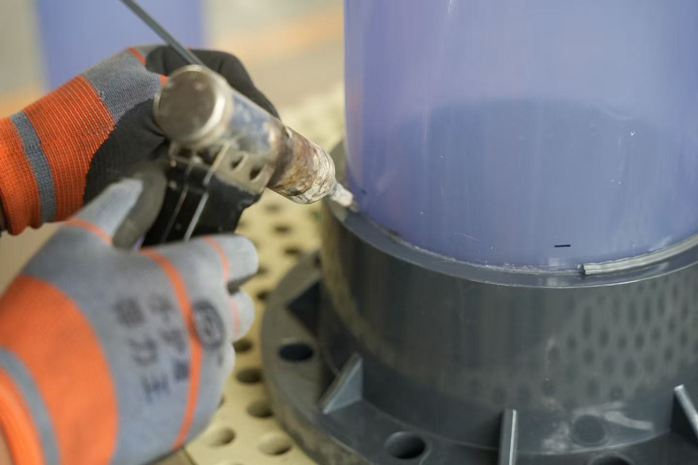 Gloved worker hands holding a plastic welding tool at a component joint